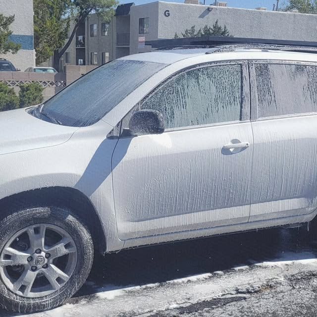 Foam pre-soak covering the door and window of a white SUV during a mobile exterior wash in Albuquerque